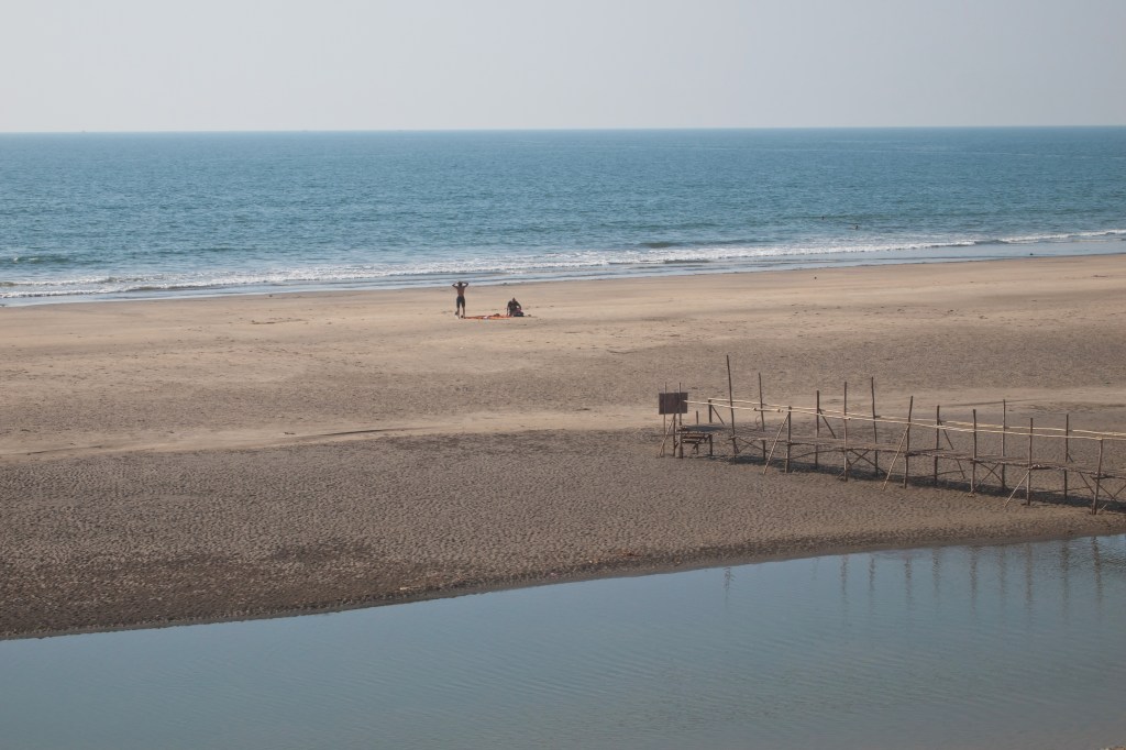 Wide view of Mandrem Beach in North Goa, with pale sand and the sea beyond the Mandrem River.